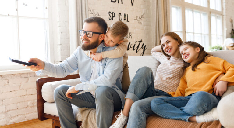 Delighted,Family,Parents,And,Kids,Smiling,While,Sitting,On,Sofa